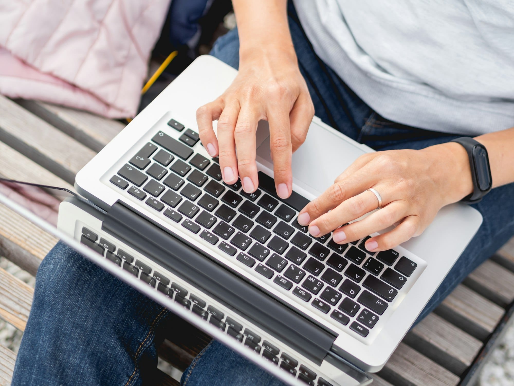 Woman sits with laptop on urban park bench. Freelancer at work. Blogger writes an article.
